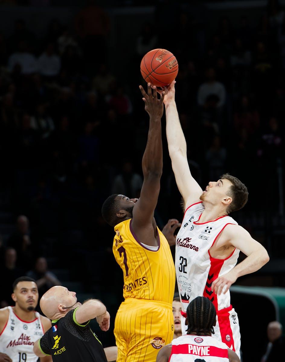 Two basketball players jump for the ball at the start of a thrilling game.